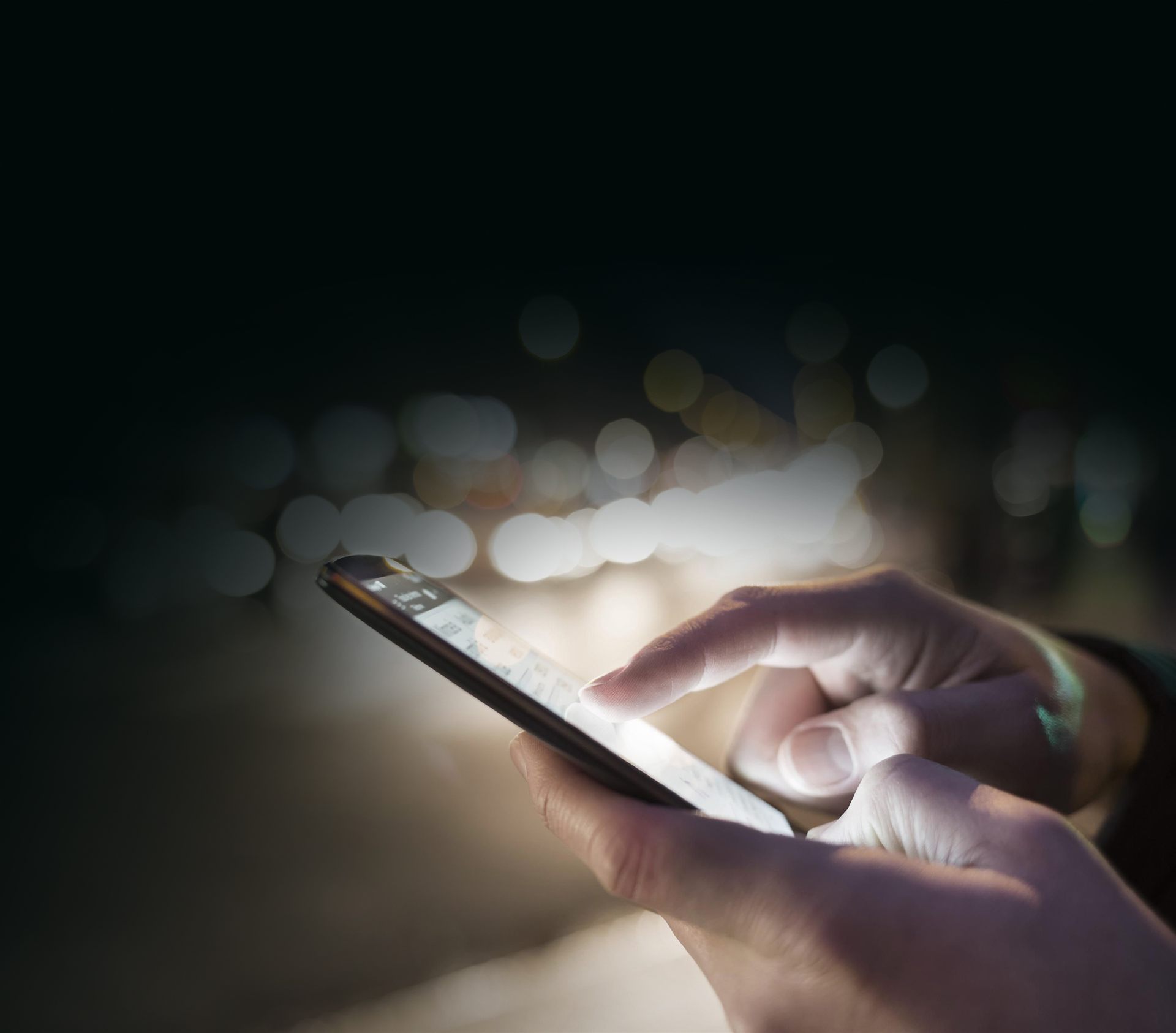 Hands using a mobile phone against city lights at night