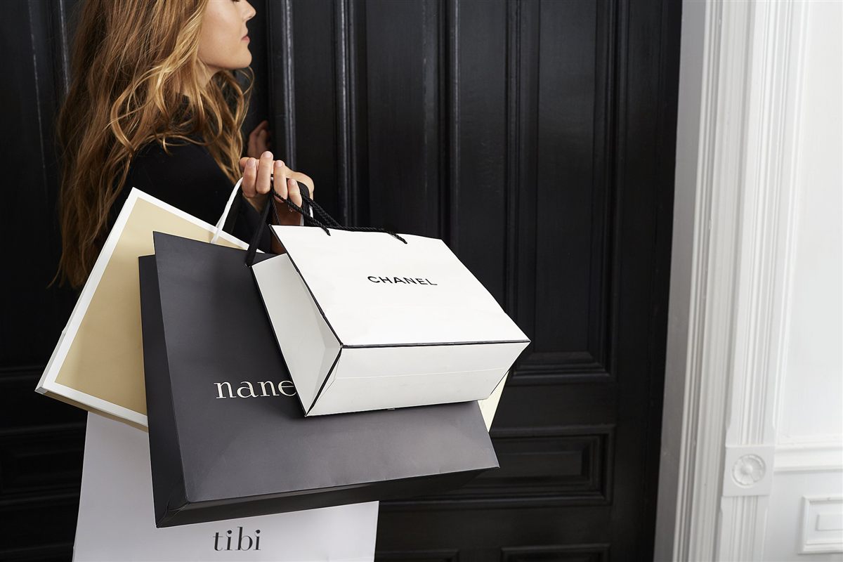 A woman carrying designer shopping bags through a grand doorway